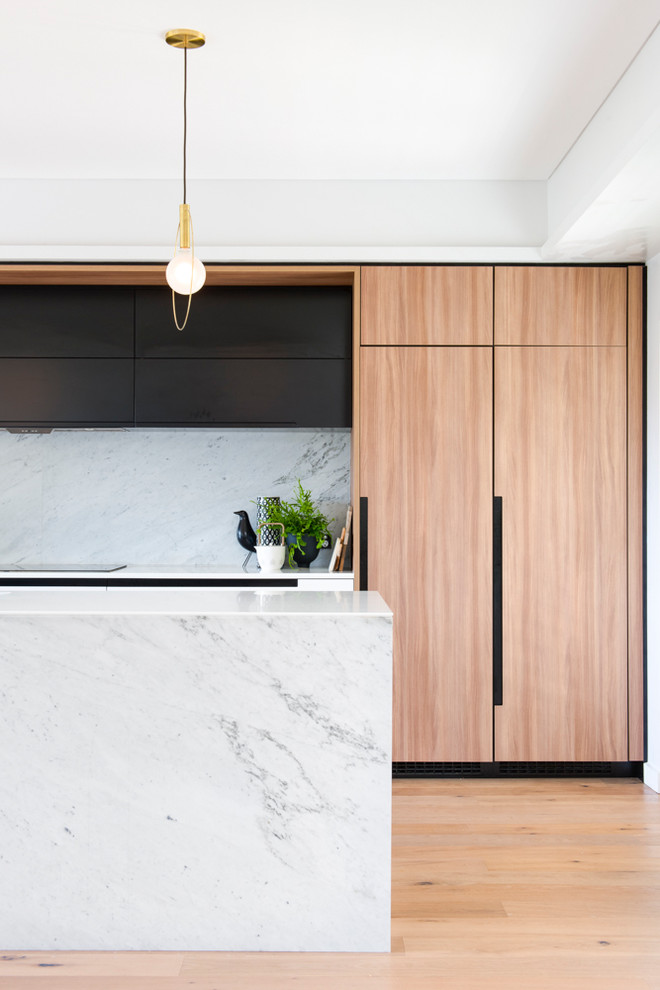 This is an example of a mid-sized contemporary galley kitchen pantry in Sydney with an undermount sink, light wood cabinets, solid surface benchtops, white splashback, marble splashback, stainless steel appliances, light hardwood floors and with island.