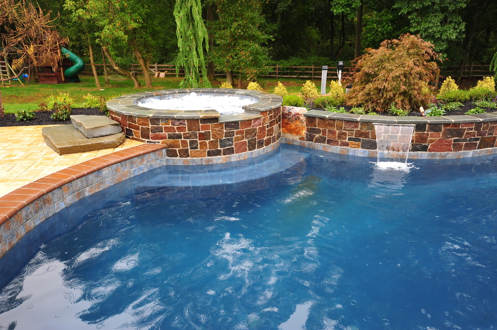 Photo of an expansive traditional backyard custom-shaped lap pool in New York with a hot tub and tile.