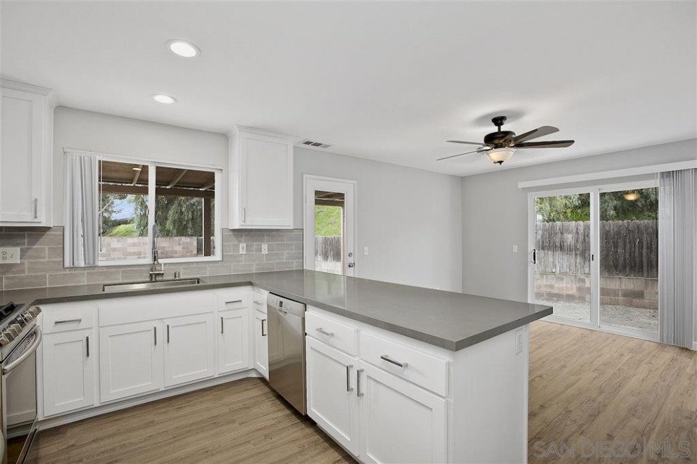 Inspiration for a mid-sized country u-shaped open plan kitchen in San Diego with an undermount sink, shaker cabinets, white cabinets, quartz benchtops, grey splashback, subway tile splashback, stainless steel appliances, vinyl floors, a peninsula, beige floor and grey benchtop.