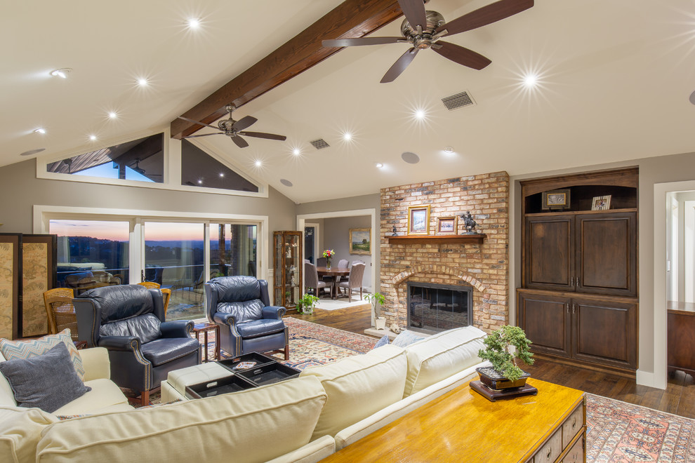 Inspiration for a large traditional family room in Austin with beige walls, medium hardwood floors, a standard fireplace, a brick fireplace surround and a concealed tv.