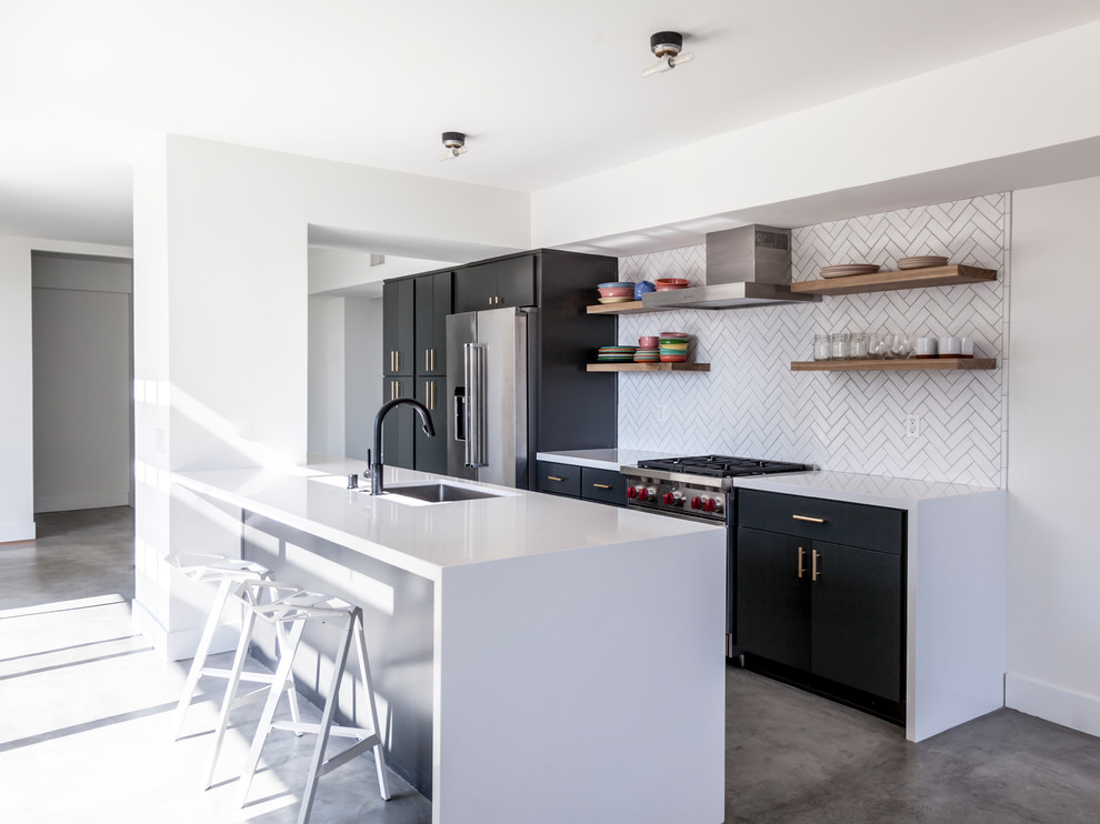 Mid-sized contemporary galley kitchen in Los Angeles with an undermount sink, flat-panel cabinets, quartz benchtops, white splashback, ceramic splashback, stainless steel appliances, concrete floors, with island, grey floor and black cabinets.