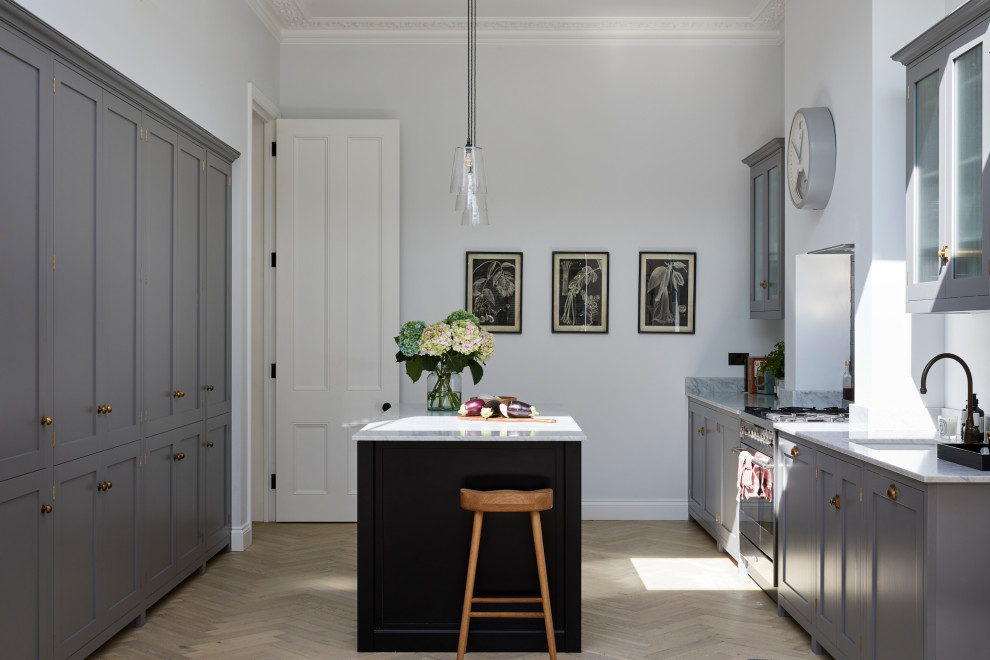 This is an example of a mid-sized transitional open plan kitchen in London with an undermount sink, shaker cabinets, grey cabinets, marble benchtops, light hardwood floors and with island.