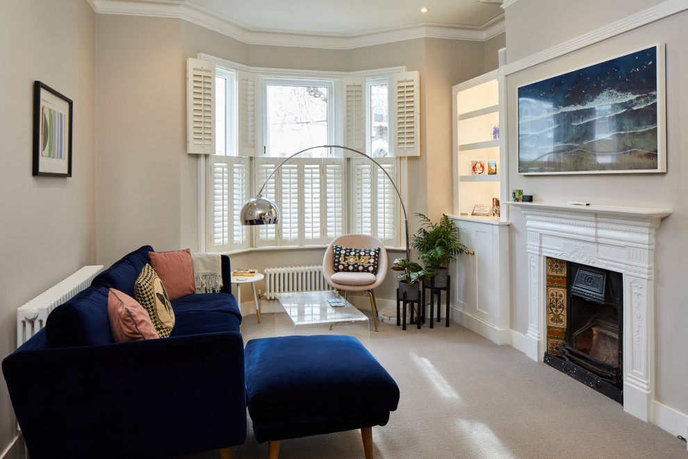 This is an example of a medium sized traditional living room in London with beige walls, carpet, a standard fireplace, a tiled fireplace surround, a wall mounted tv and beige floors.