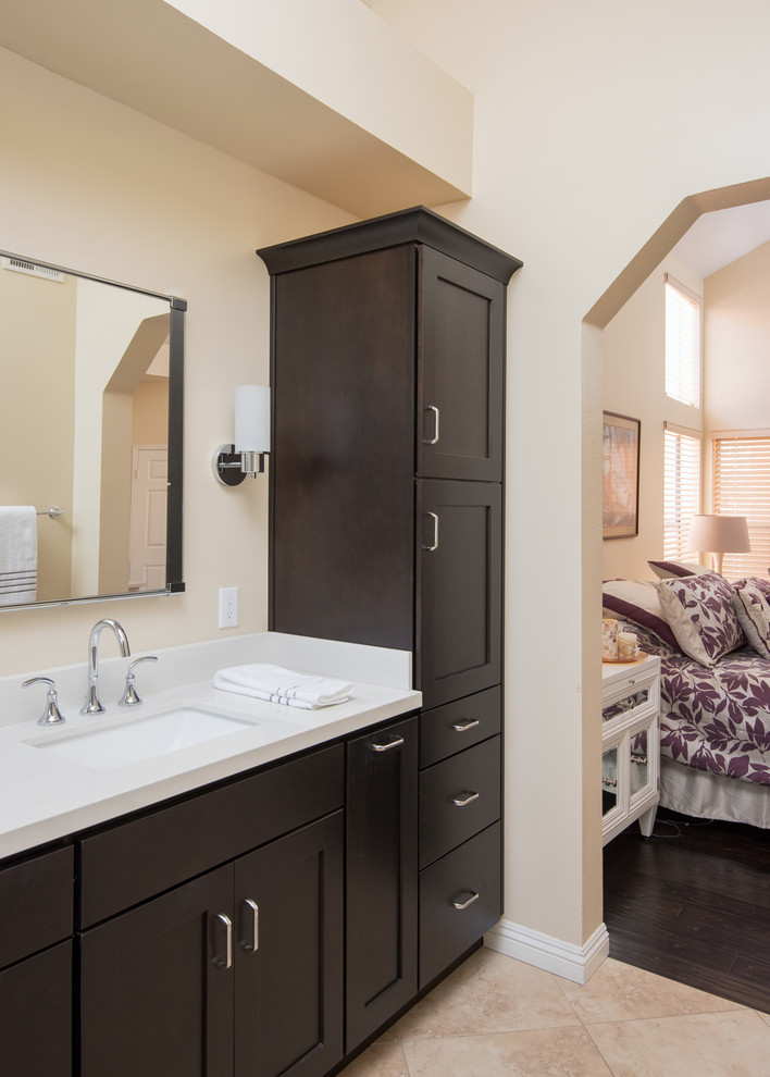 Photo of a large mediterranean master bathroom in San Diego with raised-panel cabinets, dark wood cabinets, a drop-in tub, a corner shower, a two-piece toilet, beige tile, porcelain tile, beige walls, ceramic floors, an undermount sink, engineered quartz benchtops, beige floor and a hinged shower door.