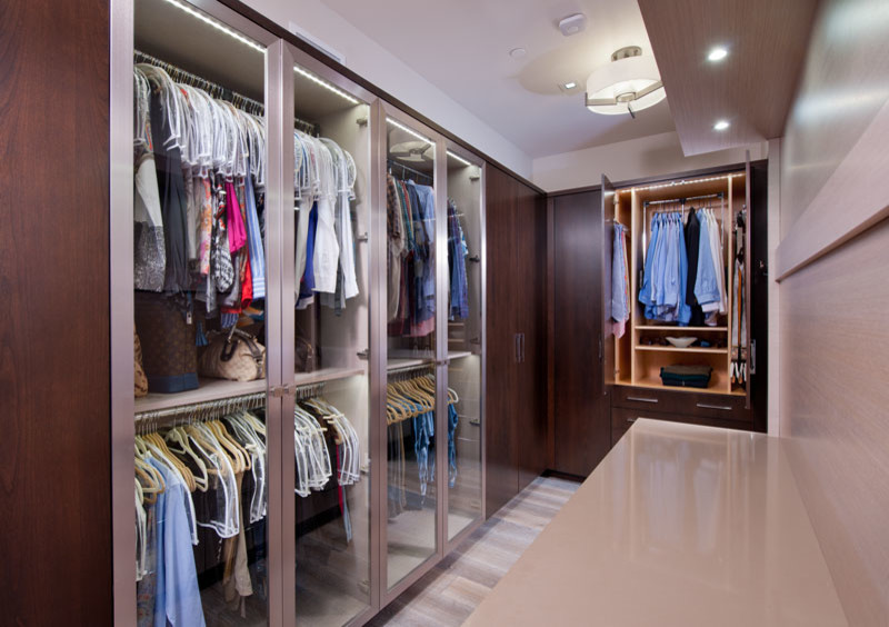 Design ideas for a small contemporary gender-neutral dressing room in Other with glass-front cabinets, dark wood cabinets, light hardwood floors and grey floor.