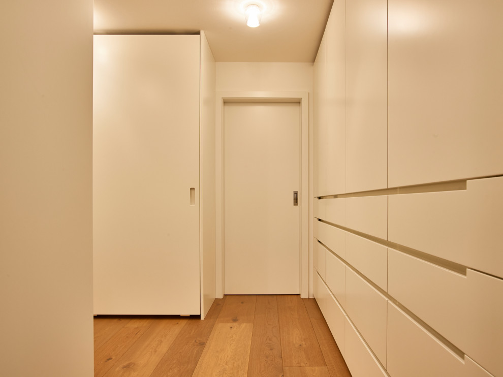 Expansive contemporary gender-neutral walk-in wardrobe in Munich with recessed-panel cabinets, white cabinets, light hardwood floors, brown floor and recessed.