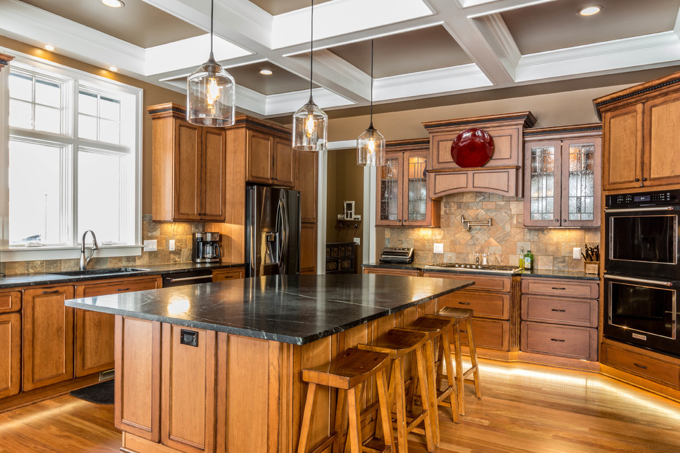 Photo of a large arts and crafts u-shaped eat-in kitchen in Detroit with an undermount sink, flat-panel cabinets, light wood cabinets, soapstone benchtops, green splashback, slate splashback, black appliances, medium hardwood floors and with island.