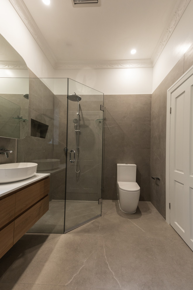 Photo of a medium sized contemporary ensuite bathroom in Sydney with freestanding cabinets, dark wood cabinets, a freestanding bath, a corner shower, a one-piece toilet, grey tiles, stone tiles, grey walls, cement flooring, engineered stone worktops, grey floors, a hinged door, white worktops, a wall niche, a single sink, a floating vanity unit and a vessel sink.