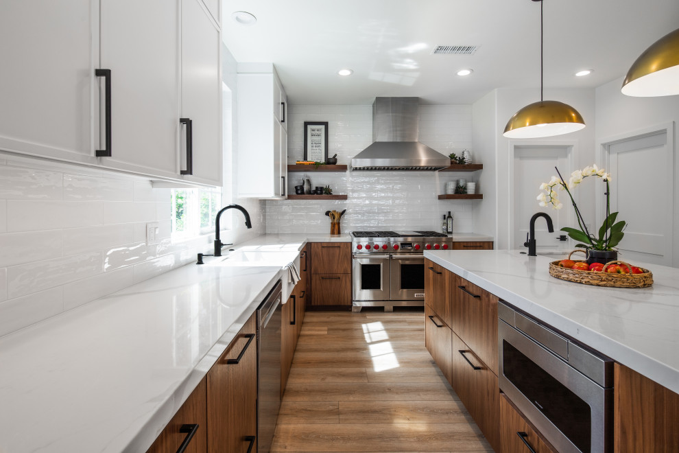 Mid-sized midcentury u-shaped open plan kitchen in San Diego with a farmhouse sink, flat-panel cabinets, medium wood cabinets, marble benchtops, white splashback, ceramic splashback, stainless steel appliances, laminate floors, with island, beige floor and white benchtop.