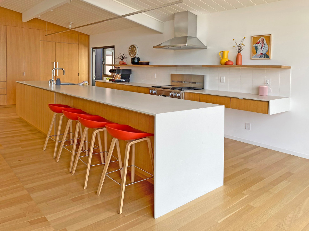 This is an example of a mid-sized midcentury eat-in kitchen in San Francisco with white splashback, stainless steel appliances, with island, white benchtop, quartz benchtops, light hardwood floors, light wood cabinets and exposed beam.