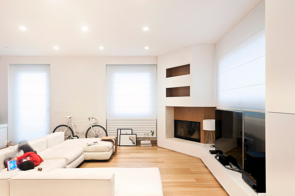 This is an example of a scandinavian family room in Cagliari with white walls, light hardwood floors, a freestanding tv, a wood fireplace surround and a corner fireplace.