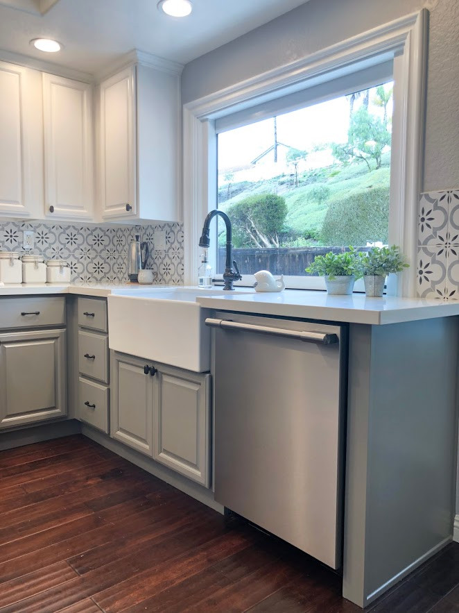 Inspiration for a small traditional u-shaped kitchen in San Diego with a farmhouse sink, raised-panel cabinets, white cabinets, quartz benchtops, white splashback, porcelain splashback, stainless steel appliances, dark hardwood floors, brown floor and white benchtop.