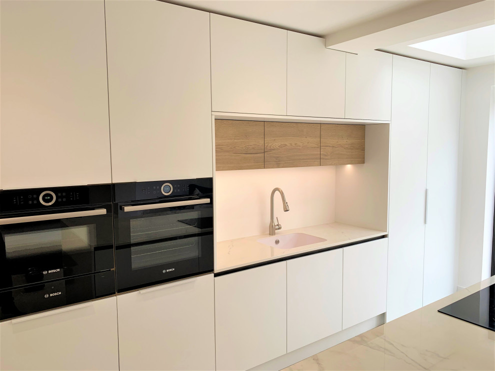 This is an example of a mid-sized contemporary single-wall eat-in kitchen in Other with an integrated sink, flat-panel cabinets, medium wood cabinets, solid surface benchtops, black appliances, vinyl floors, with island and white benchtop.