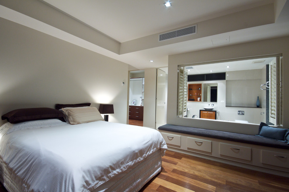 Design ideas for a large contemporary master bedroom in Townsville with beige walls and medium hardwood floors.