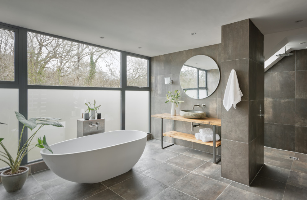 This is an example of a large contemporary master bathroom with an open shower, gray tile, porcelain floors, wood benchtops, grey floor, an open shower, a single vanity and a freestanding vanity.