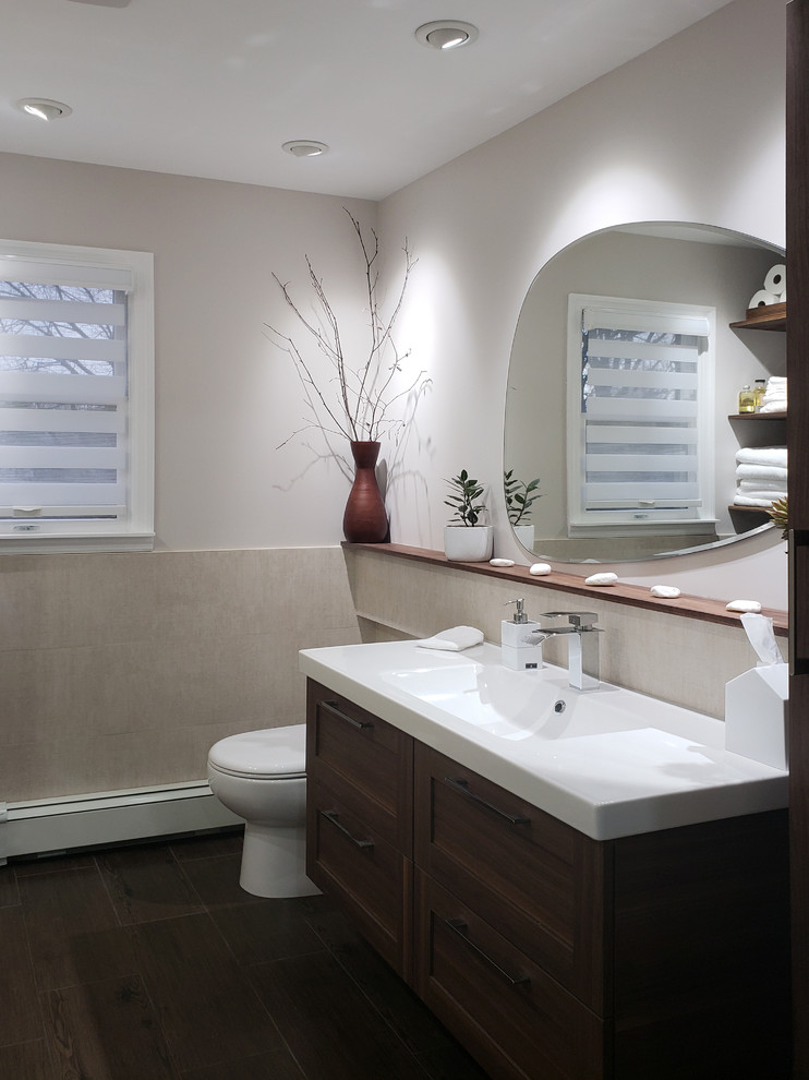 Photo of a small transitional kids bathroom in New York with shaker cabinets, medium wood cabinets, an alcove tub, a one-piece toilet, beige tile, porcelain tile, beige walls, porcelain floors, an integrated sink, solid surface benchtops and brown floor.