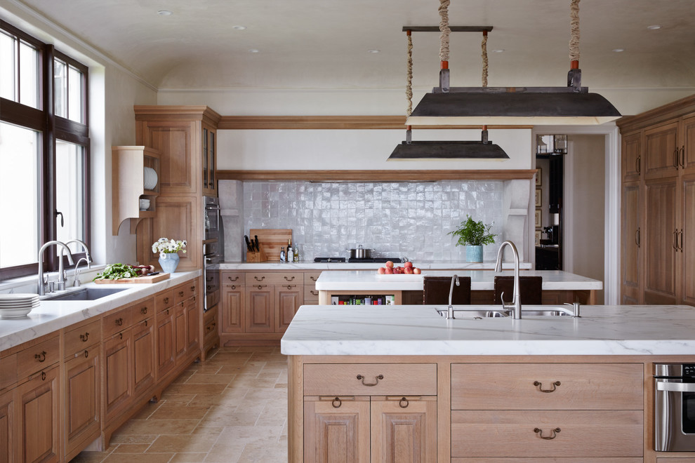 Inspiration for a mediterranean kitchen in Jacksonville with a double-bowl sink, raised-panel cabinets, light wood cabinets, white splashback, stainless steel appliances, travertine floors and multiple islands.