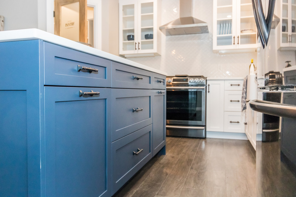 Kitchen - mid-sized l-shaped vinyl floor and brown floor kitchen idea with a farmhouse sink, recessed-panel cabinets, blue cabinets, quartzite countertops, white backsplash, ceramic backsplash, stainless steel appliances, an island and white countertops
