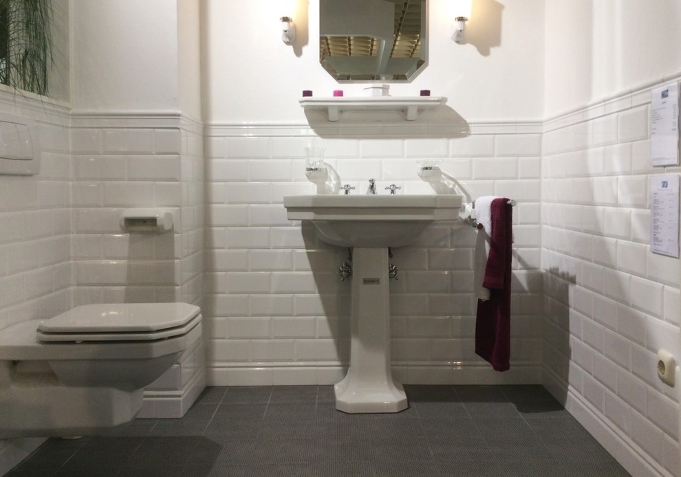 This is an example of a small traditional powder room in Munich with a wall-mount toilet, white tile, subway tile, white walls, ceramic floors, a pedestal sink and grey floor.