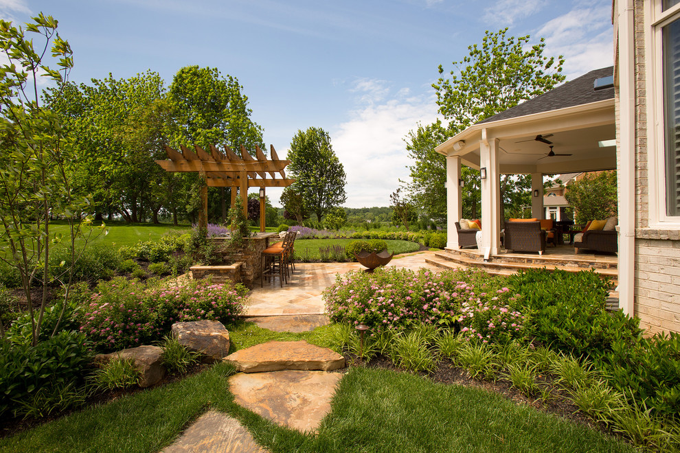 This is an example of a transitional backyard verandah in DC Metro with natural stone pavers and a roof extension.