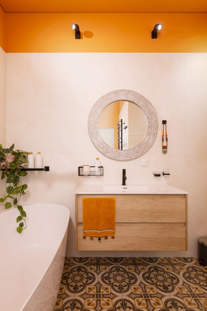 Пример оригинального дизайна: ванная комната среднего размера в стиле фьюжн с плоскими фасадами, светлыми деревянными фасадами, отдельно стоящей ванной, душем без бортиков, инсталляцией, бежевой плиткой, керамогранитной плиткой, оранжевыми стенами, полом из керамической плитки, душевой кабиной, накладной раковиной, столешницей из искусственного камня, разноцветным полом, душем с распашными дверями, белой столешницей, гигиеническим душем, тумбой под одну раковину и подвесной тумбой