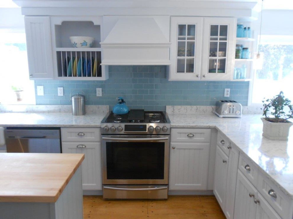 Large beach style u-shaped eat-in kitchen in Portland Maine with a farmhouse sink, louvered cabinets, white cabinets, marble benchtops, blue splashback, subway tile splashback, stainless steel appliances, medium hardwood floors and with island.
