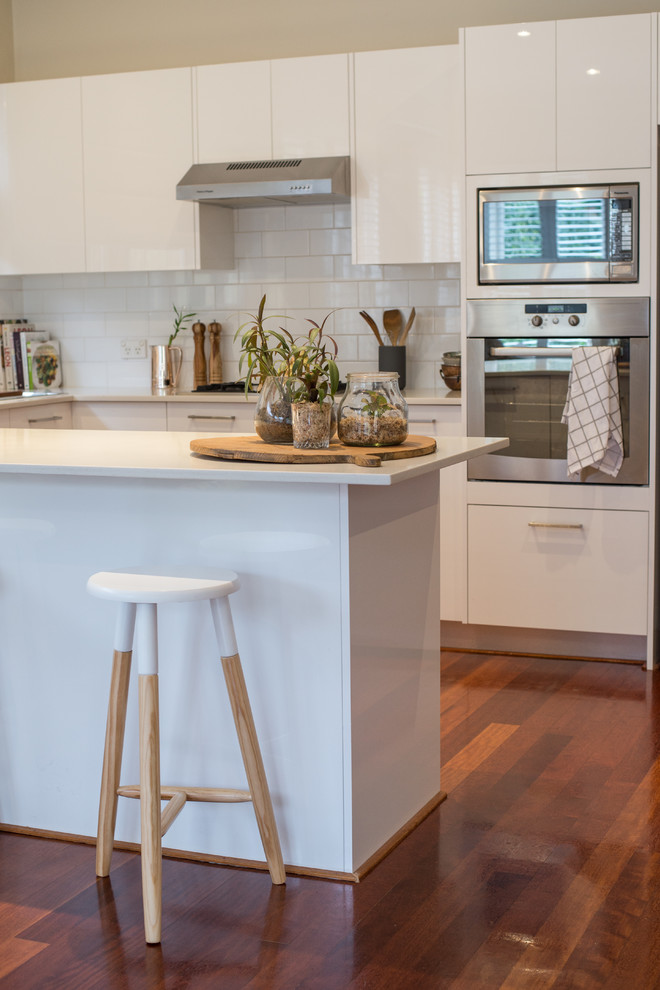 Mid-sized contemporary u-shaped eat-in kitchen in Sydney with a double-bowl sink, flat-panel cabinets, white cabinets, granite benchtops, white splashback, ceramic splashback, stainless steel appliances, dark hardwood floors and with island.