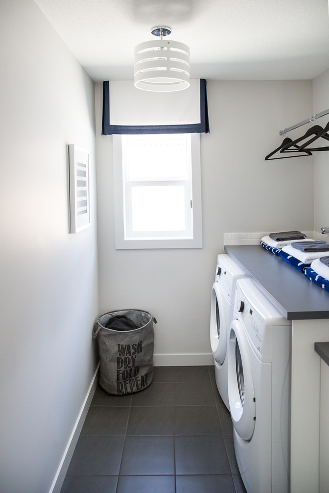 Design ideas for a mid-sized contemporary galley dedicated laundry room in Calgary with flat-panel cabinets, white cabinets, quartz benchtops, white walls, ceramic floors, a side-by-side washer and dryer and grey floor.