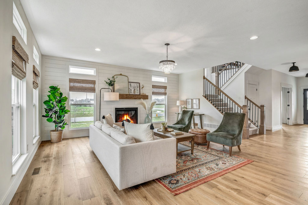 Large country open concept living room in Columbus with white walls, a standard fireplace and light hardwood floors.