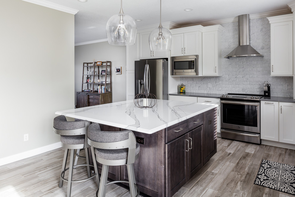Example of a mid-sized transitional l-shaped ceramic tile and gray floor eat-in kitchen design with an undermount sink, shaker cabinets, white cabinets, quartz countertops, white backsplash, marble backsplash, stainless steel appliances, an island and gray countertops