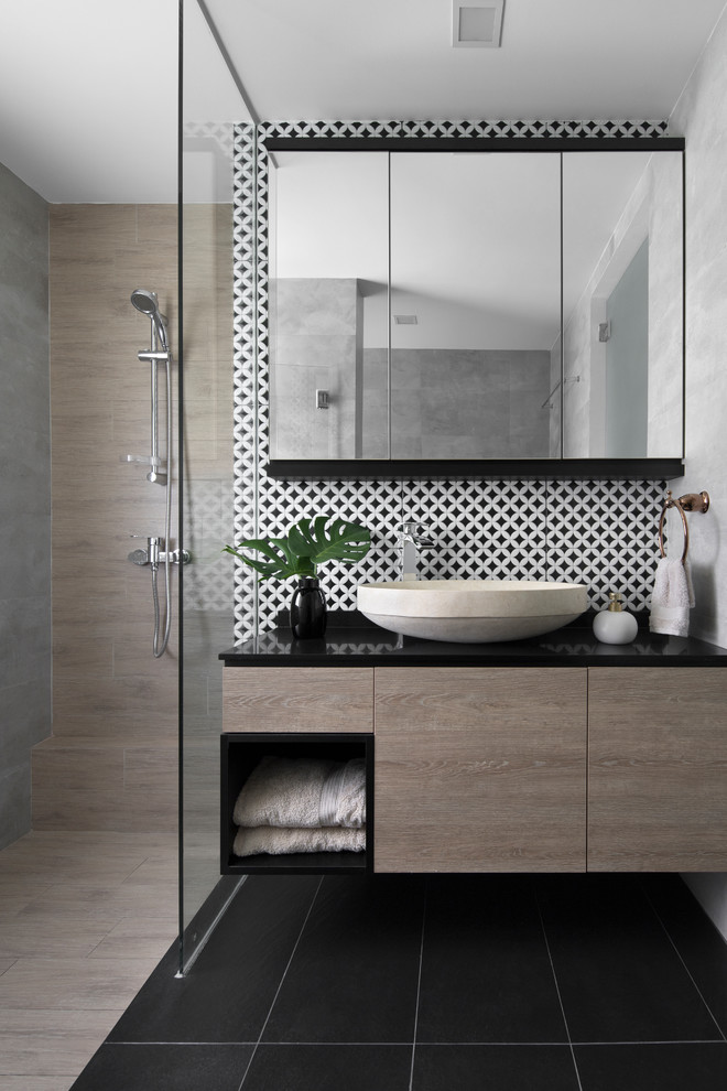 Contemporary bathroom in Singapore with flat-panel cabinets, light wood cabinets, a curbless shower, black and white tile, brown tile, gray tile, grey walls, a vessel sink, black floor, an open shower and black benchtops.