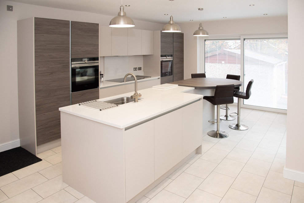 Design ideas for a large contemporary single-wall open plan kitchen in Sussex with an integrated sink, flat-panel cabinets, white cabinets, laminate benchtops, grey splashback, black appliances, laminate floors, with island and grey benchtop.