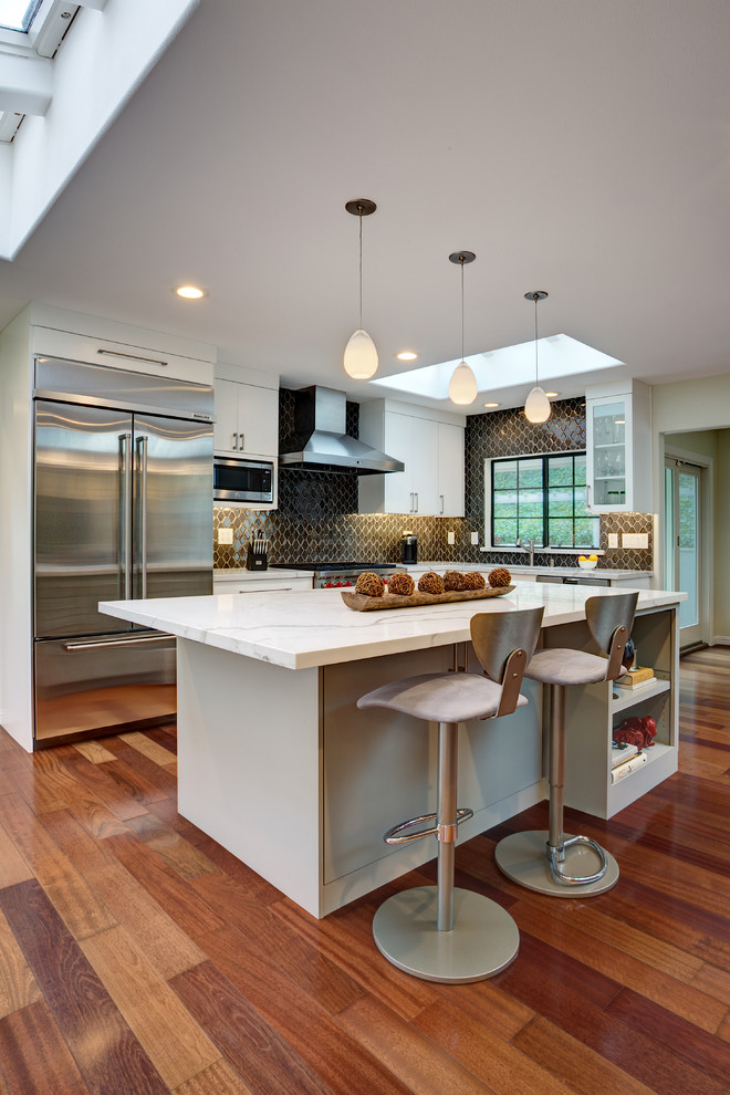 Mid-sized contemporary l-shaped open plan kitchen in San Francisco with an undermount sink, flat-panel cabinets, white cabinets, quartz benchtops, grey splashback, ceramic splashback, stainless steel appliances, medium hardwood floors, with island and red floor.