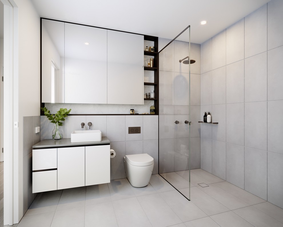 Design ideas for a modern 3/4 bathroom in Melbourne with ceramic floors, a vessel sink, granite benchtops, an open shower, flat-panel cabinets, white cabinets, an open shower, a wall-mount toilet, gray tile, grey walls and grey floor.