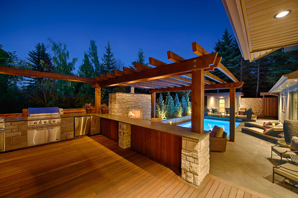 This is an example of a large traditional backyard deck in Calgary with an outdoor kitchen and a pergola.