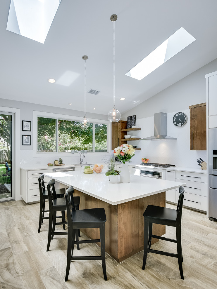 This is an example of a large contemporary u-shaped open plan kitchen in Austin with an undermount sink, flat-panel cabinets, white cabinets, quartzite benchtops, white splashback, subway tile splashback, stainless steel appliances, ceramic floors, with island and brown floor.