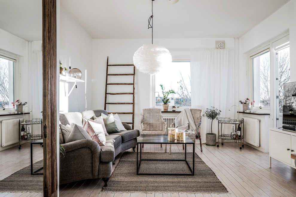 Inspiration for a mid-sized scandinavian enclosed family room in Gothenburg with white walls, light hardwood floors, beige floor and a freestanding tv.