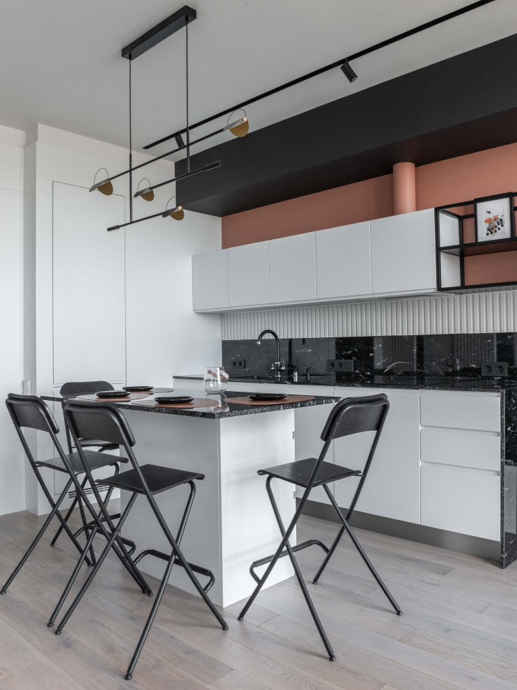 Small scandinavian single-wall eat-in kitchen in Moscow with an undermount sink, flat-panel cabinets, white cabinets, granite benchtops, black splashback, granite splashback, black appliances, light hardwood floors, with island, grey floor and black benchtop.