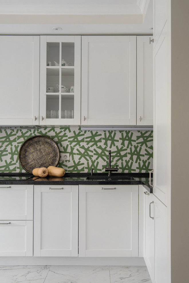 Mid-sized eclectic l-shaped eat-in kitchen in Moscow with an integrated sink, raised-panel cabinets, white cabinets, solid surface benchtops, green splashback, cement tile splashback, stainless steel appliances, porcelain floors, no island, white floor and black benchtop.