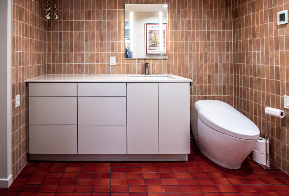 На фото: главная ванная комната среднего размера в стиле ретро с плоскими фасадами, бежевыми фасадами, ванной в нише, душем без бортиков, унитазом-моноблоком, коричневой плиткой, керамической плиткой, бежевыми стенами, полом из керамической плитки, врезной раковиной, столешницей из искусственного кварца, красным полом, душем с распашными дверями, бежевой столешницей, нишей, тумбой под одну раковину и встроенной тумбой с