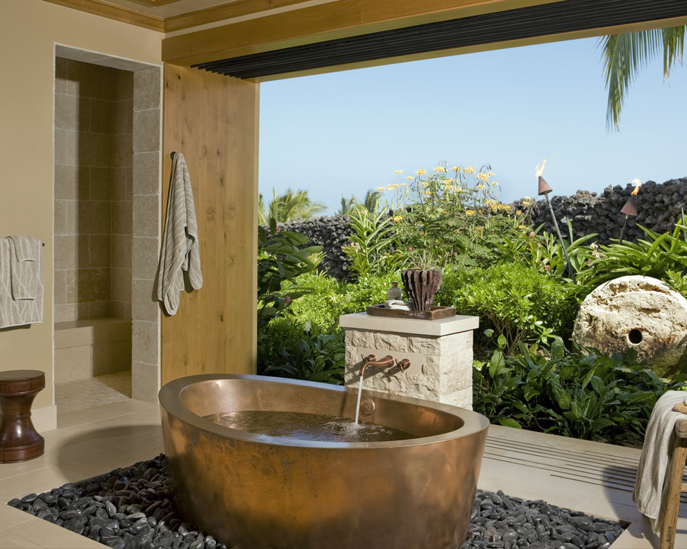 Tropical bathroom in Hawaii with a freestanding tub, beige tile and an alcove shower.