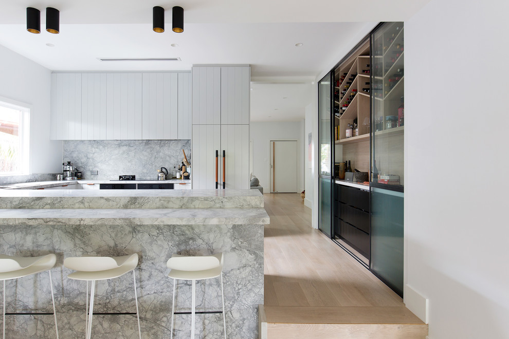 Inspiration for a contemporary u-shaped kitchen in Sydney with white cabinets, grey splashback, panelled appliances, light hardwood floors, a peninsula, beige floor and grey benchtop.