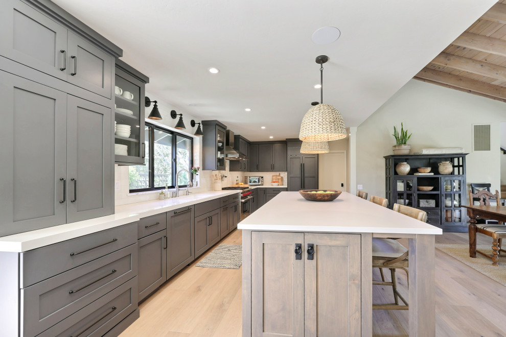 Example of a mid-sized transitional l-shaped laminate floor open concept kitchen design with a double-bowl sink, flat-panel cabinets, gray cabinets, quartz countertops, white backsplash, ceramic backsplash, stainless steel appliances, an island and white countertops