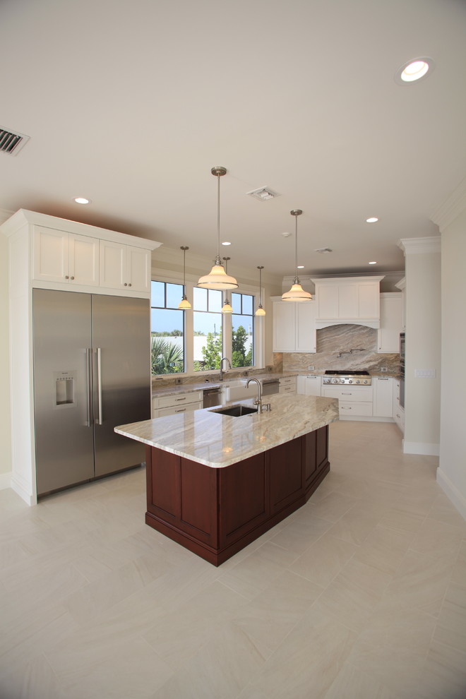 This is an example of a large beach style u-shaped open plan kitchen in Miami with a farmhouse sink, recessed-panel cabinets, white cabinets, granite benchtops, beige splashback, stone slab splashback, stainless steel appliances, porcelain floors, with island and beige floor.