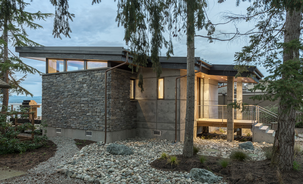 Photo of a small modern one-storey grey house exterior in Seattle with stone veneer, a shed roof and a metal roof.