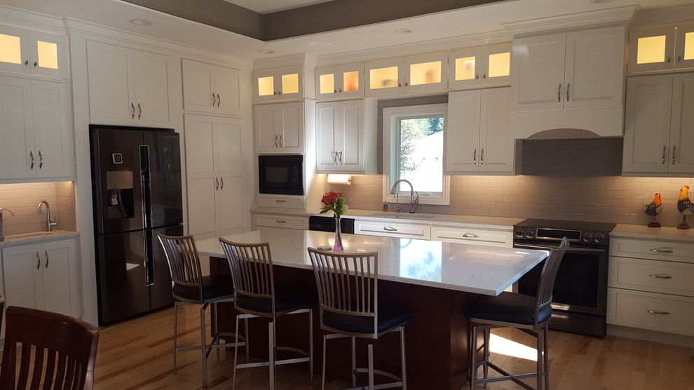 Large transitional l-shaped light wood floor eat-in kitchen photo with an undermount sink, flat-panel cabinets, white cabinets, quartz countertops, white backsplash, subway tile backsplash, stainless steel appliances, an island and white countertops
