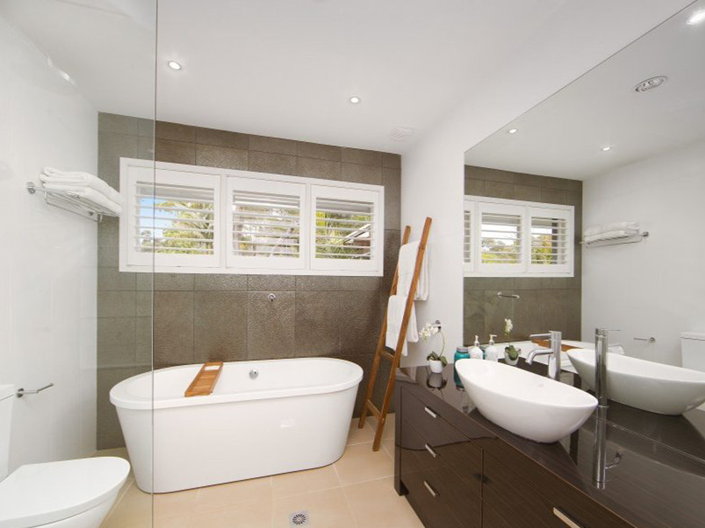 This is an example of a contemporary bathroom in Sydney with a vessel sink, flat-panel cabinets, brown cabinets, a freestanding tub, a two-piece toilet and brown tile.