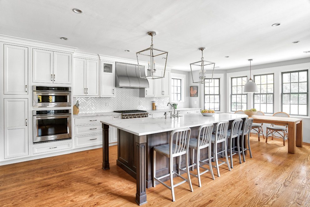 Example of a huge classic galley medium tone wood floor eat-in kitchen design in New York with a farmhouse sink, beaded inset cabinets, white cabinets, quartzite countertops, white backsplash, subway tile backsplash, stainless steel appliances, an island and white countertops