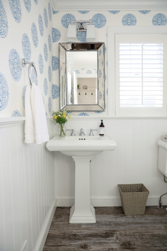 Photo of a country bathroom in New York with white cabinets, a corner shower, gray tile, blue walls, wood-look tile, grey floor, a hinged shower door, a single vanity and wallpaper.