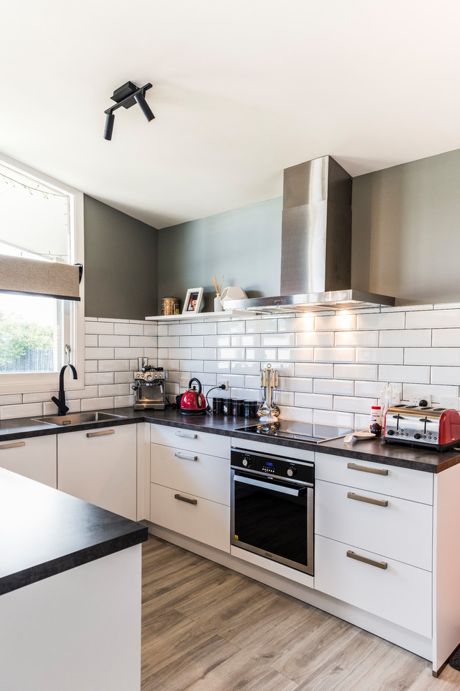 This is an example of a mid-sized modern u-shaped kitchen pantry in Christchurch with flat-panel cabinets, white cabinets, laminate benchtops, white splashback, subway tile splashback, stainless steel appliances, laminate floors, a peninsula and brown floor.